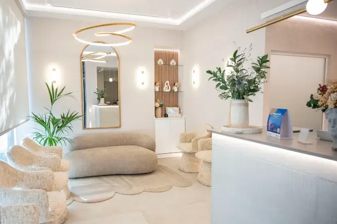 Sala de espera premium de Lúmina Clinic en Madrid con sofás y sillones en tonos beige, espejo arqueado e iluminación cálida.